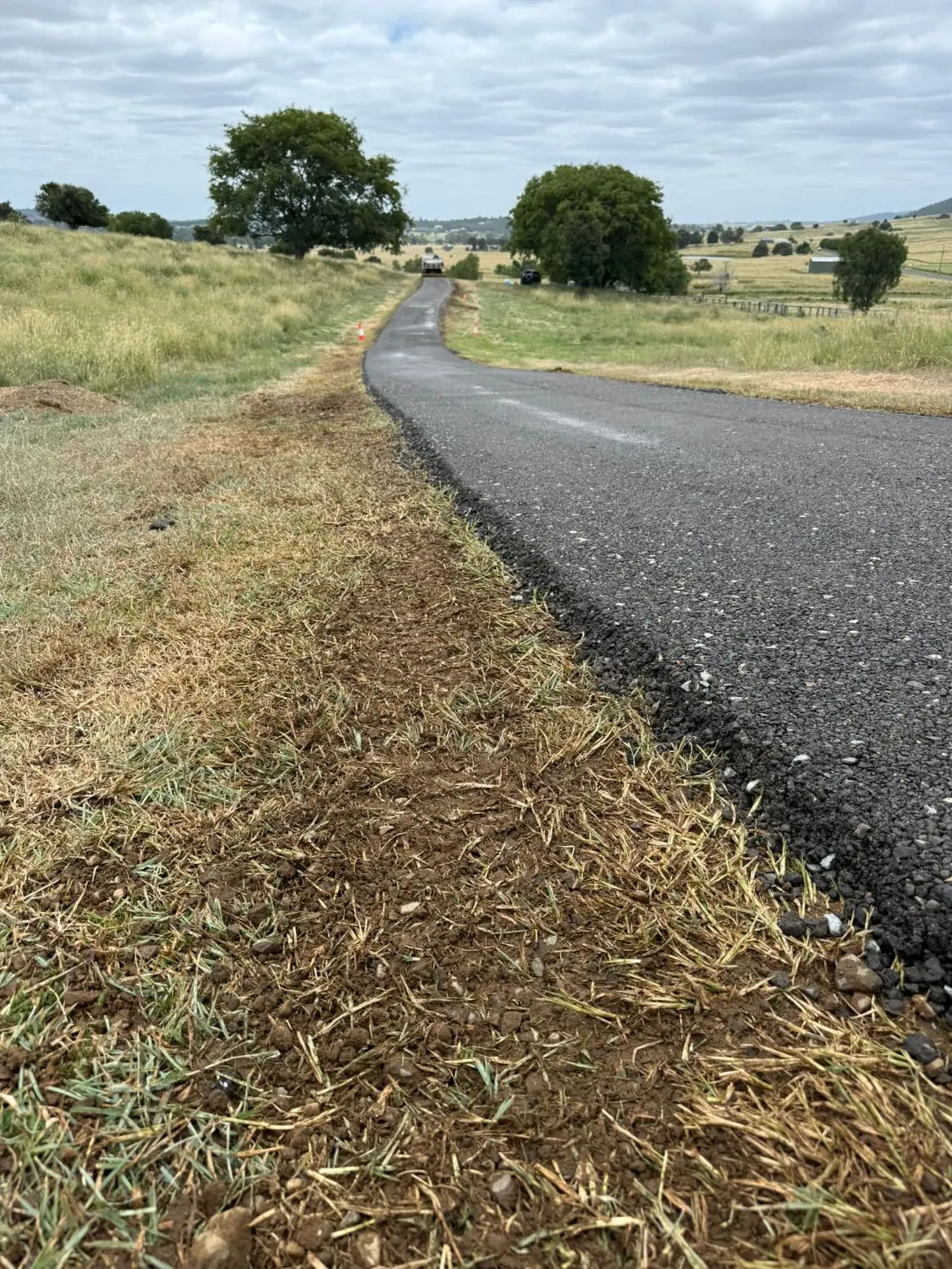 Newly paved asphalt driveway along a rural hillside